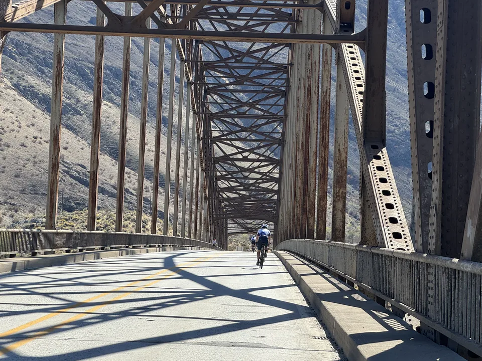 KREW riders crossing a steel bridge through mountain terrain