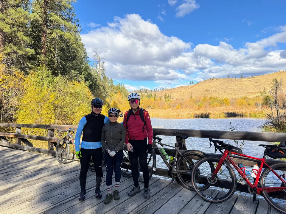 Three KREW riders with bikes beside an autumn mountain lake